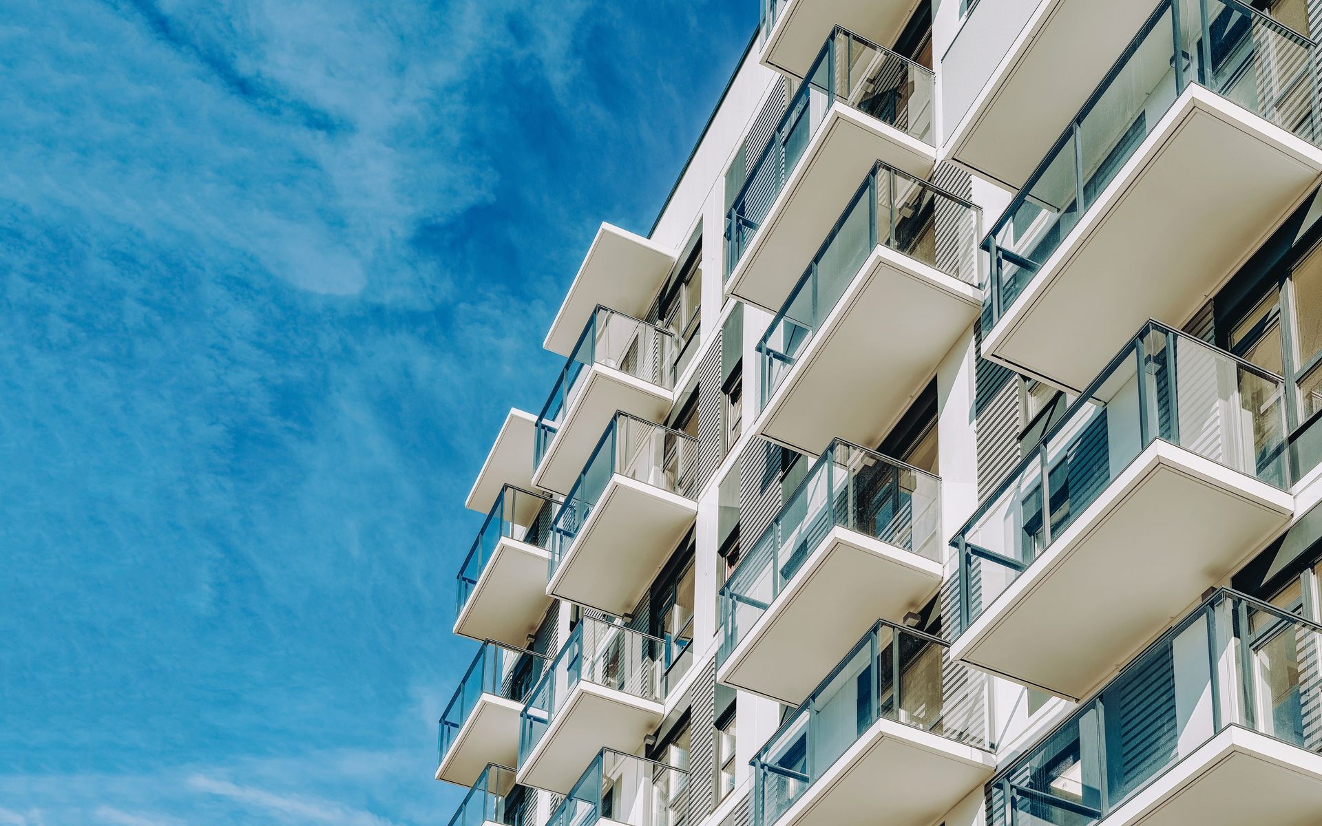 White apartment building with multiple balconies against a blue sky with wispy clouds.