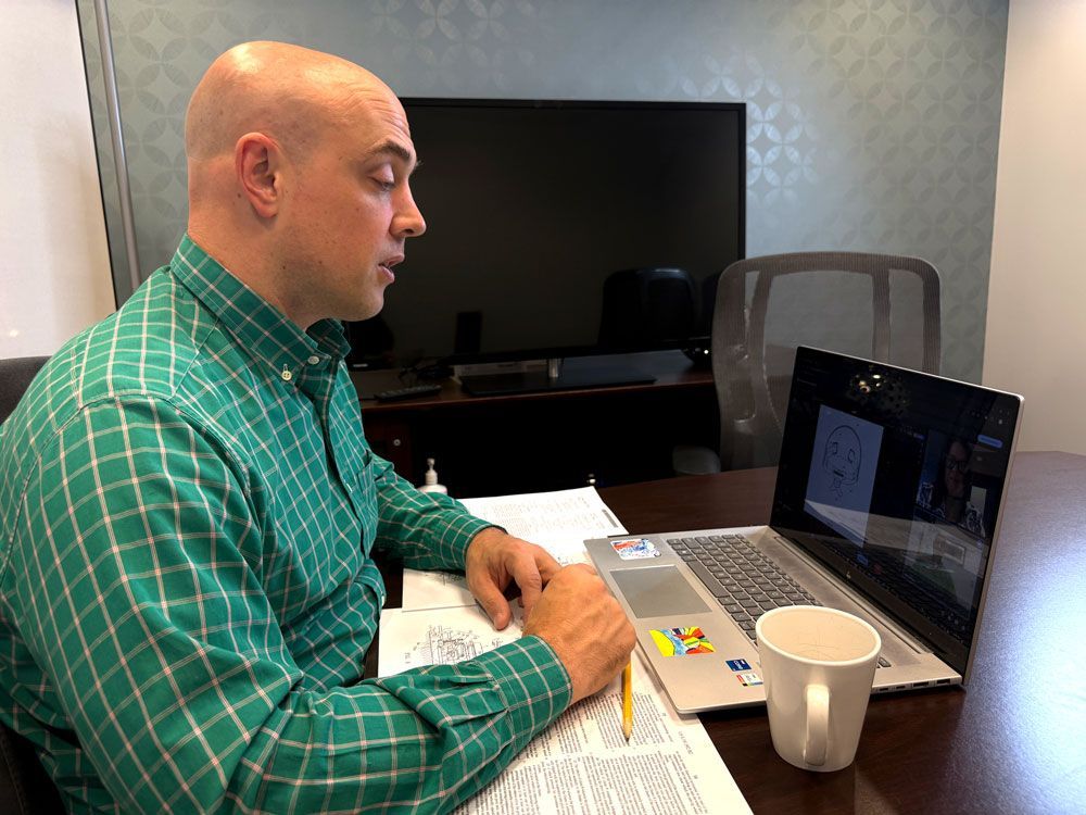 A man is sitting at a desk in front of a whiteboard.