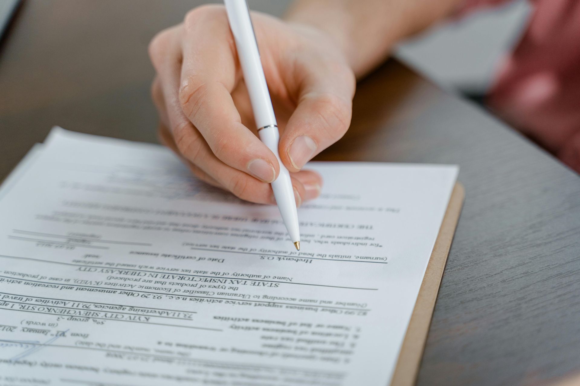 Hands signing a document with a pen on a clipboard on a desk
