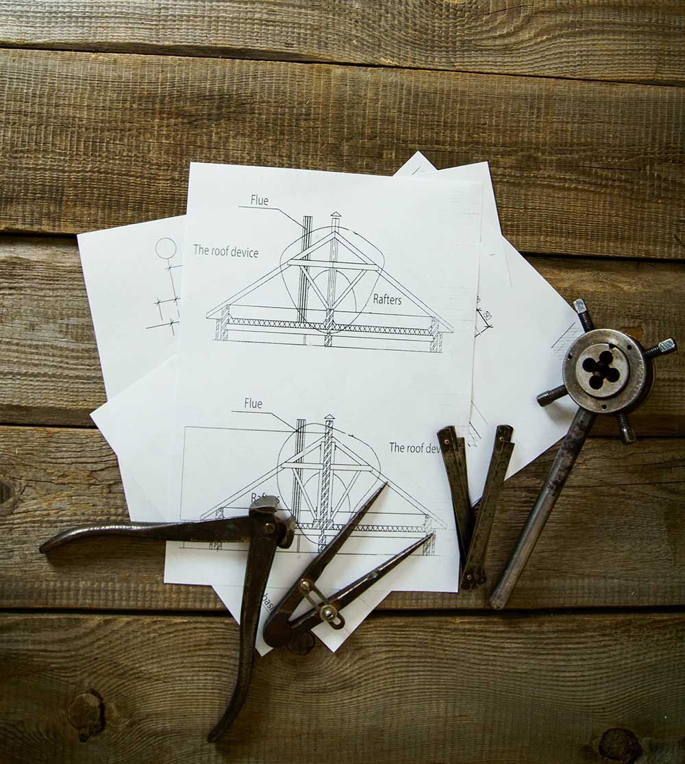 Sketches of a ship with drafting tools arranged on a rustic wooden surface.