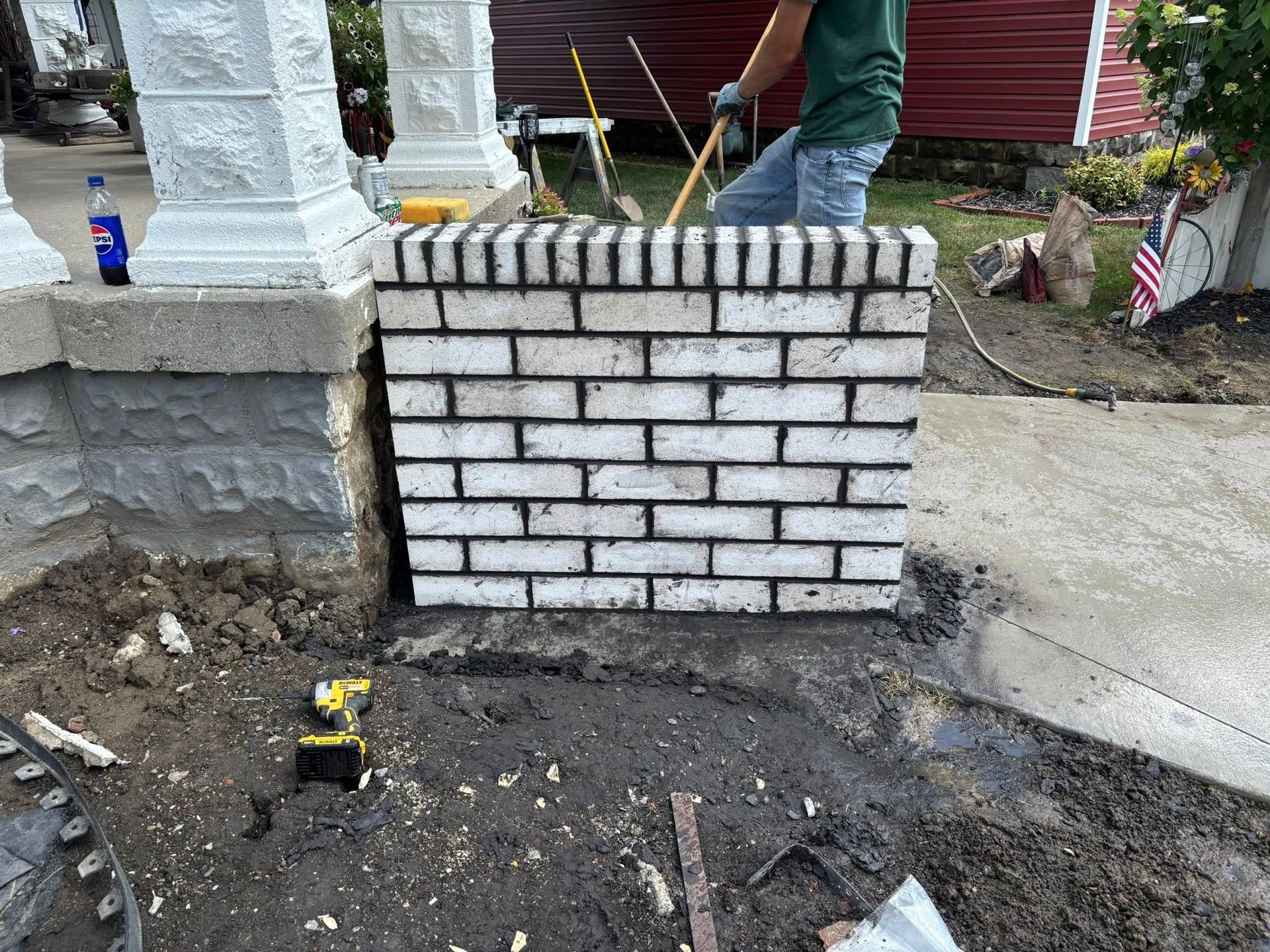 Brick column being built by a person in a yard next to a concrete porch.