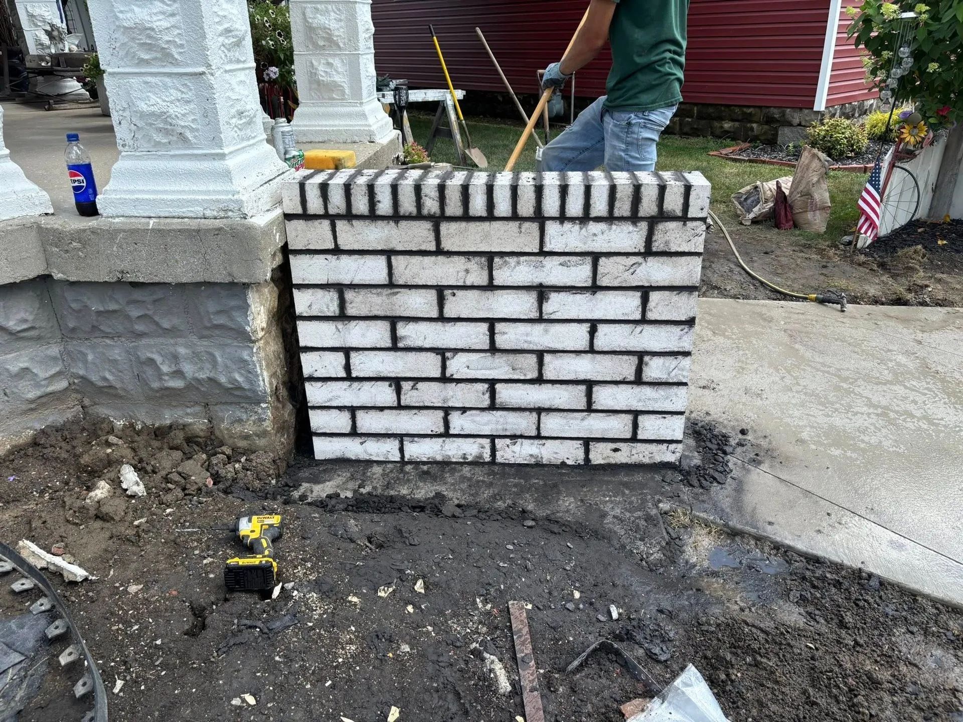 A person builds a brick wall in front of a house. White bricks, mortar, and tools are visible.