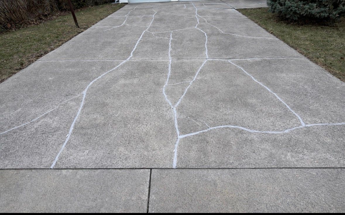 Concrete driveway with several white-chalked cracks; the driveway leads to a garage.