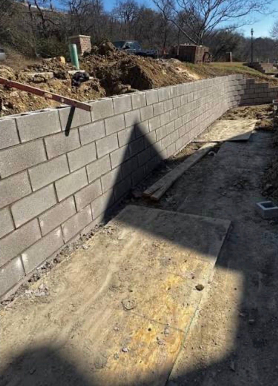 A cinder block retaining wall under construction. Dirt path in front, sunny day.