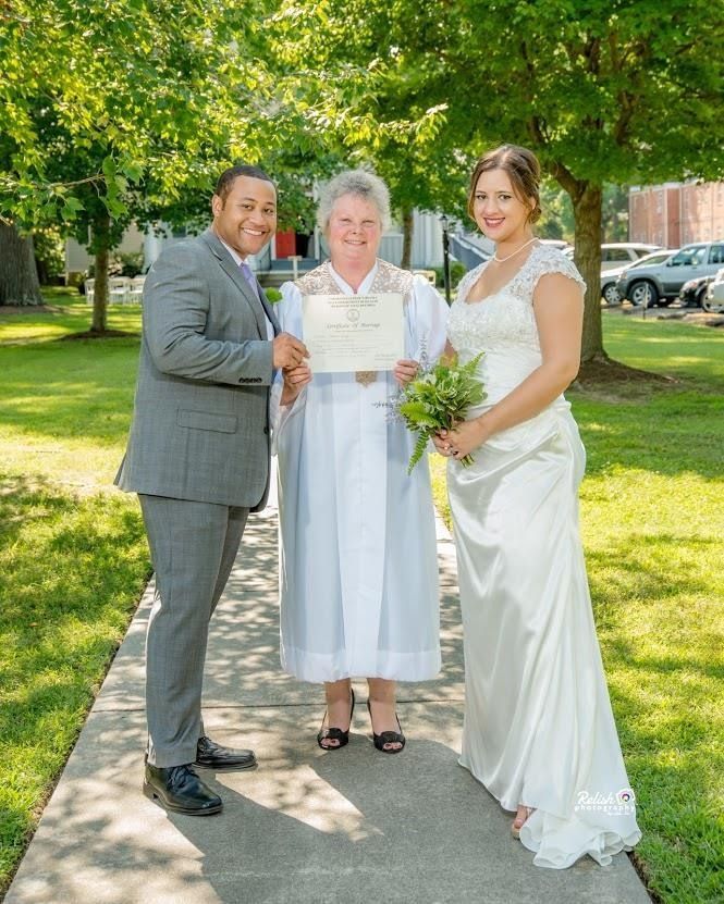 Three people posing outdoors; center person holds a certificate, flanked by two smiling companions.