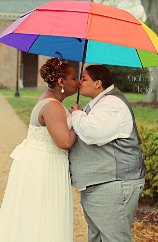 Two people sharing an umbrella on a rainy path, standing close and facing each other.