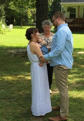 Couple exchanging vows outdoors while an officiant stands between them on a grassy lawn.