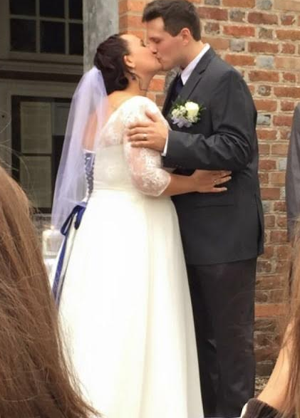 Bride and groom kissing during wedding ceremony beside a brick wall