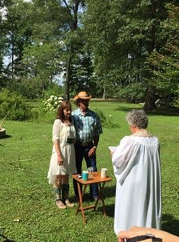 Three people stand in a sunny park beside a small table with cups and drinks.