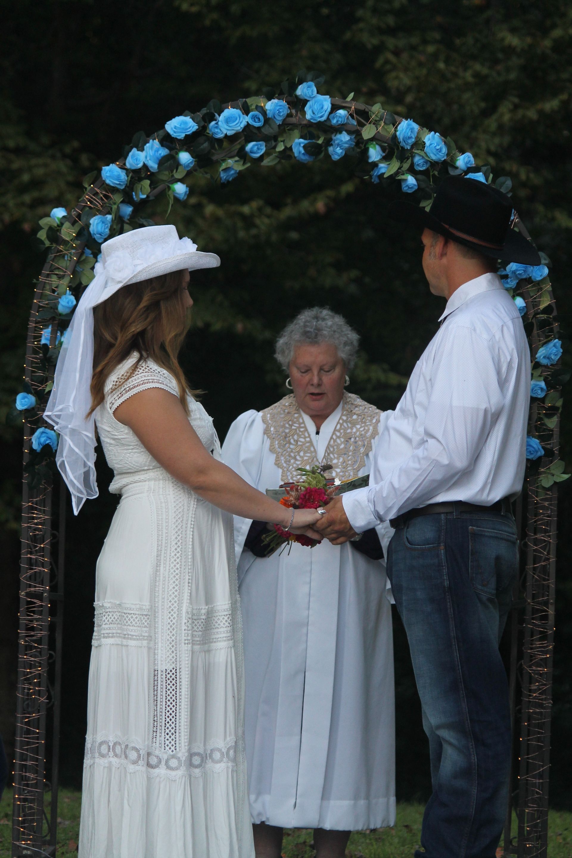 Outdoor wedding ceremony with bride and groom holding hands under a blue-flower arch