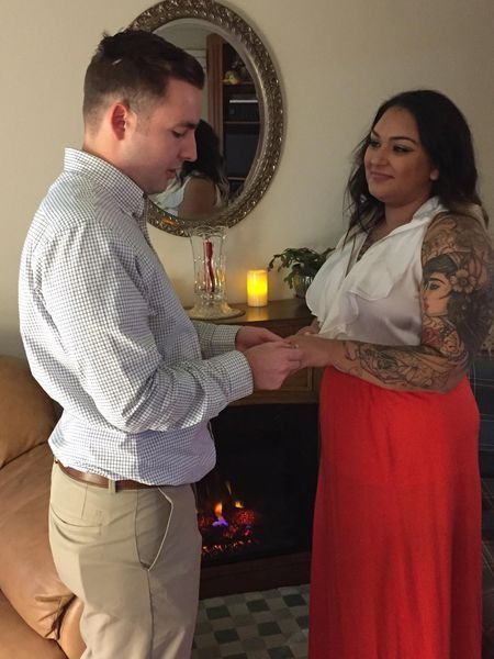 Couple holding hands before a lit fireplace, with a candle and mirror on a mantel behind them.