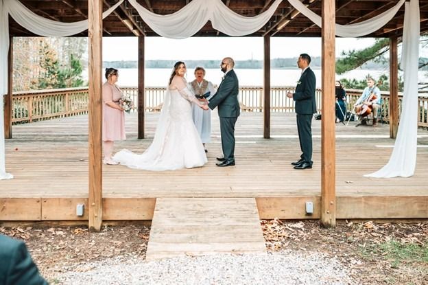 Wedding ceremony on a wooden pavilion, with the couple exchanging vows before an officiant and guests.