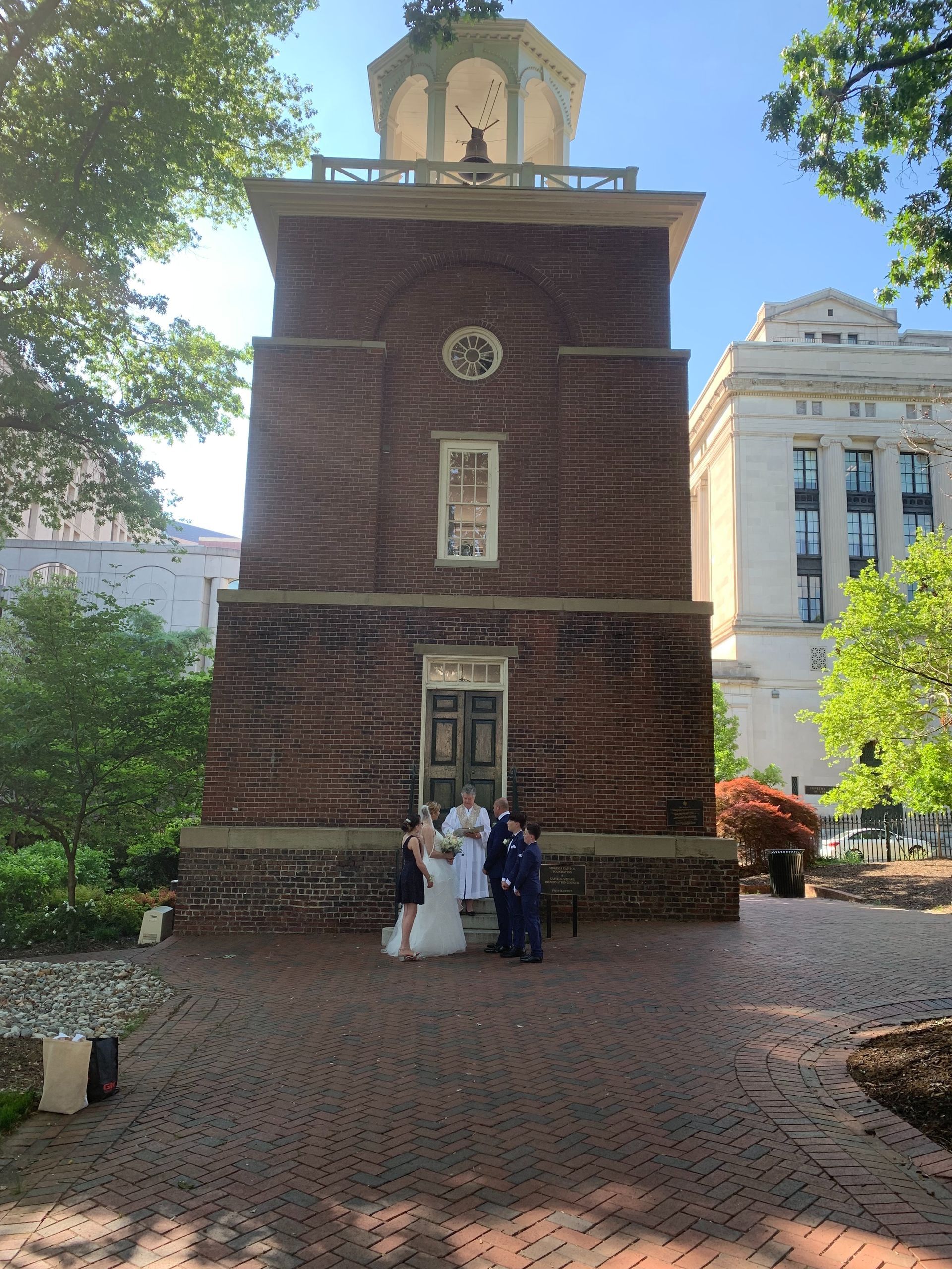 People posing in front of a brick tower with a clock, on a cobblestone courtyard under trees.
