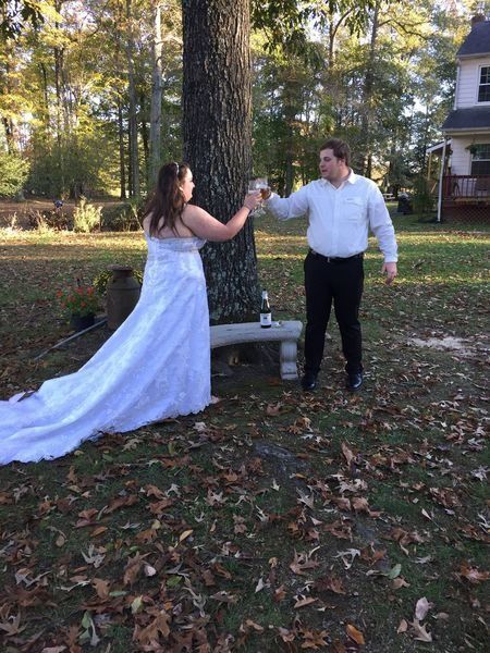 Bride and groom holding hands and dancing outdoors beside a tree in a park