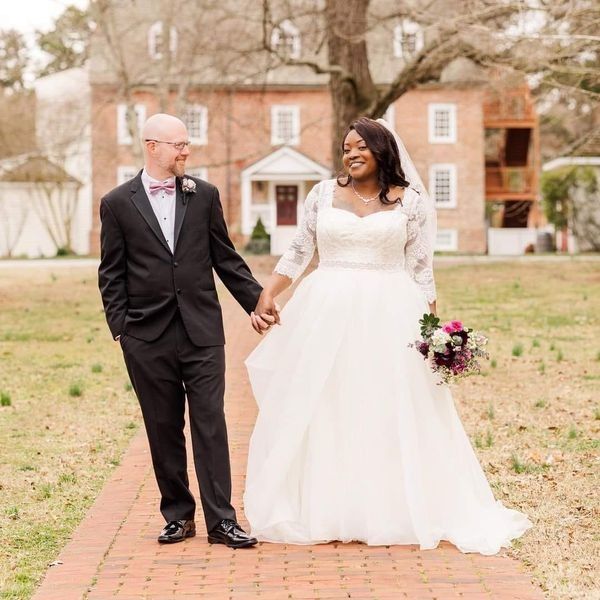 Bride and groom in wedding attire holding hands outdoors by a brick building
