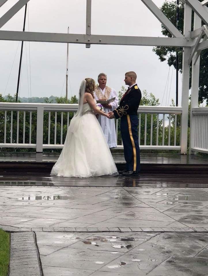 Wedding couple standing with officiant on a wet outdoor gazebo, holding hands during the ceremony