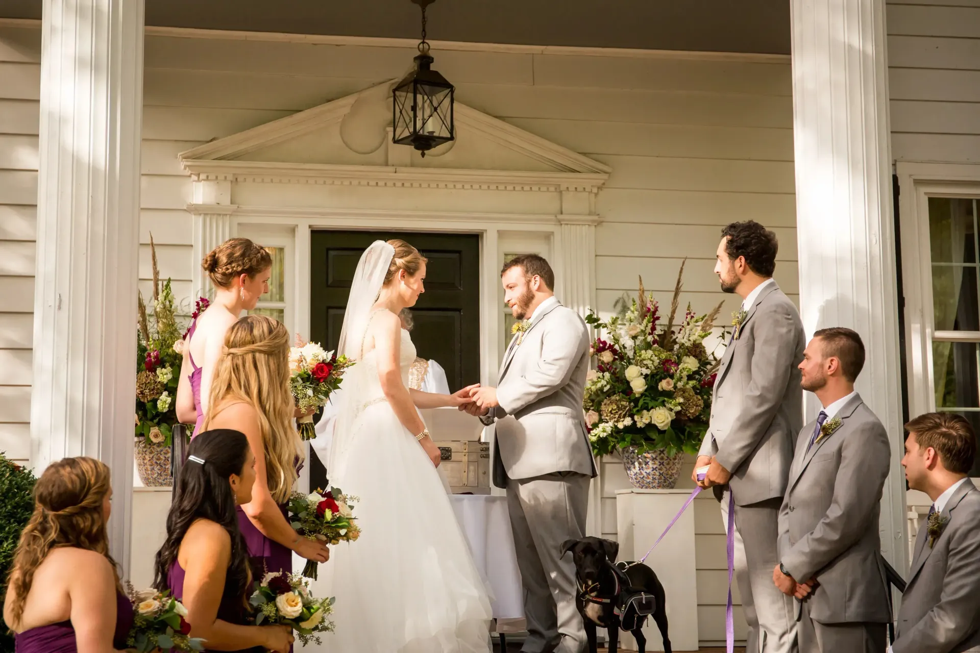 Bride and groom exchange vows at an outdoor wedding ceremony on a porch, with guests nearby