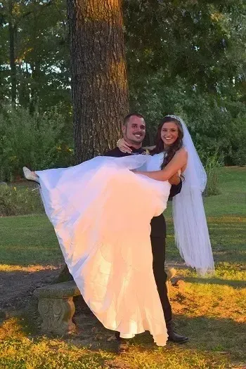 Two people holding a white sheet outdoors by a tree at sunset