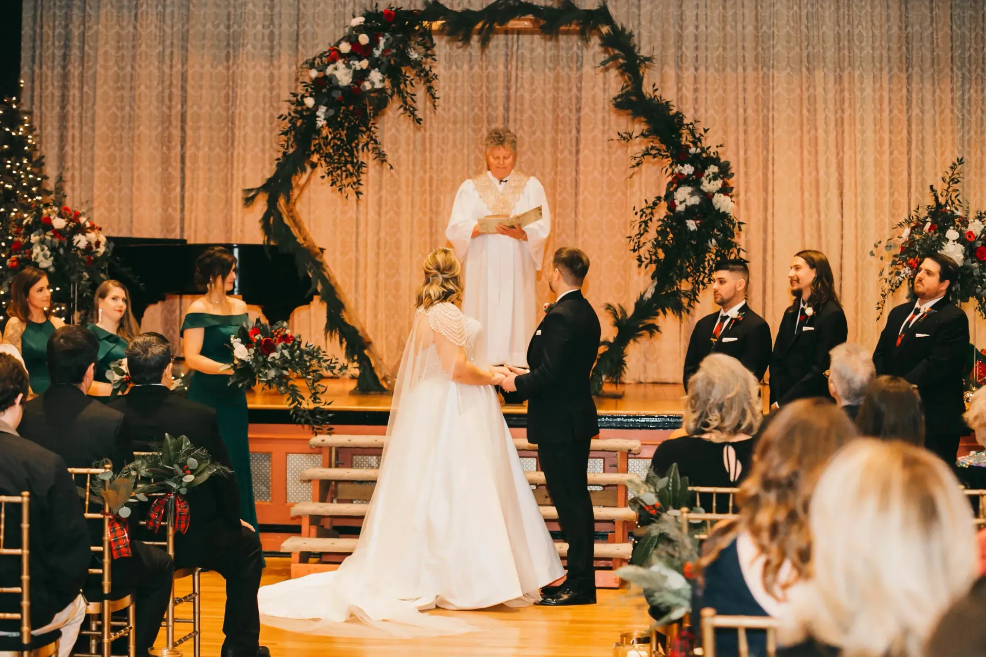 Wedding ceremony with couple at altar under floral arch, guests seated on both sides in a decorated hall