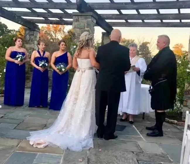 Wedding ceremony outdoors with bride, officiant, and attendants in blue and black attire