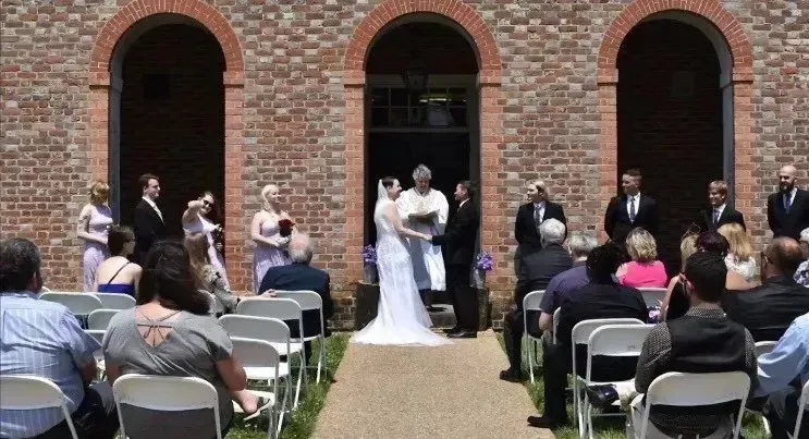 Outdoor wedding ceremony in front of a brick building with arched doorways and seated guests