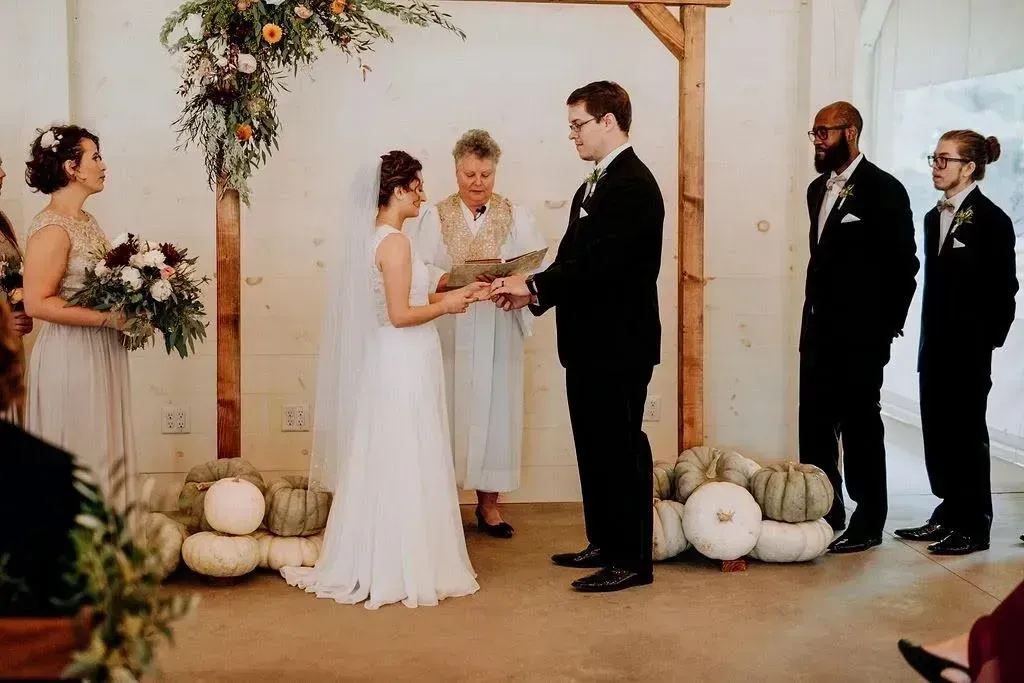 Wedding ceremony under a floral arch, with bride and groom exchanging vows beside attendants
