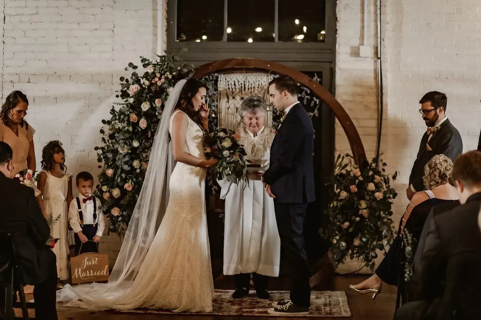 Bride and groom exchanging vows under a floral arch at an indoor wedding ceremony