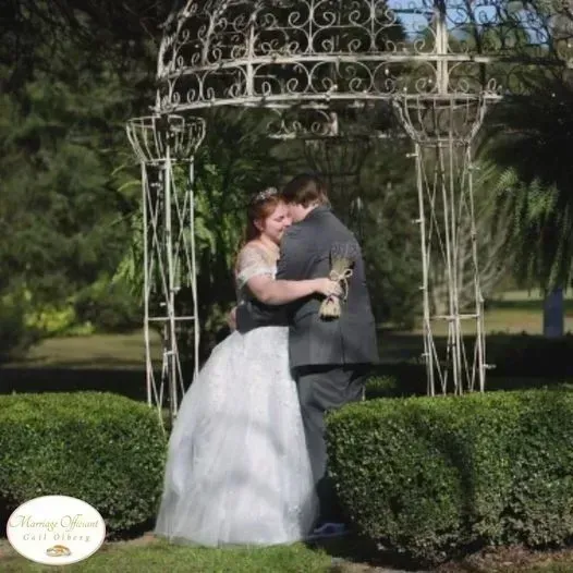 Bride and groom embracing under a white garden gazebo on a sunny day