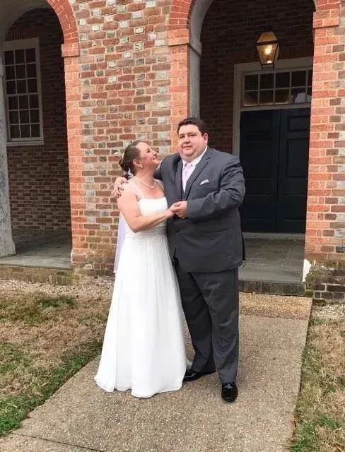Bride and groom posing together outside a brick building, smiling and holding hands