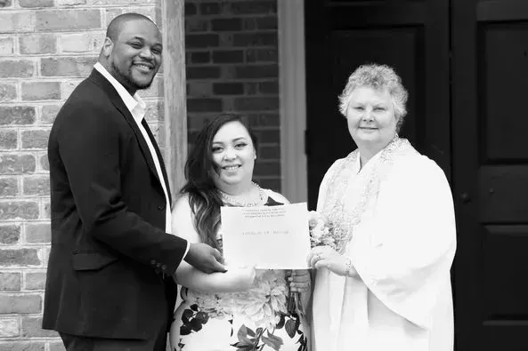 Three people posing with a certificate in front of a building entrance