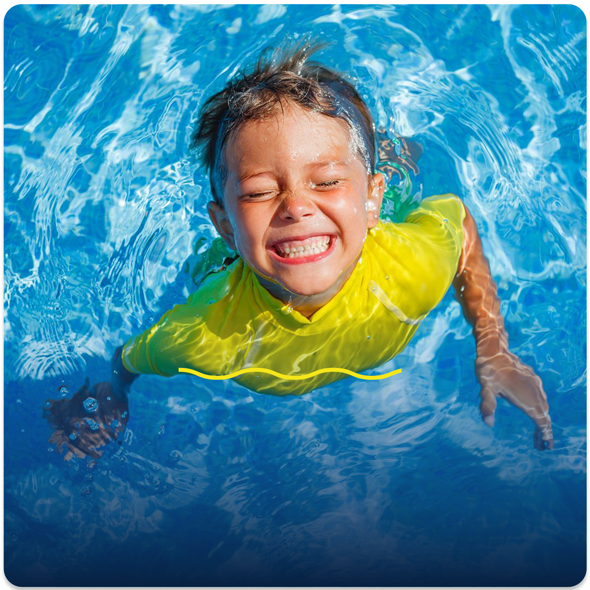 A boy in a yellow shirt is swimming in a pool and smiling