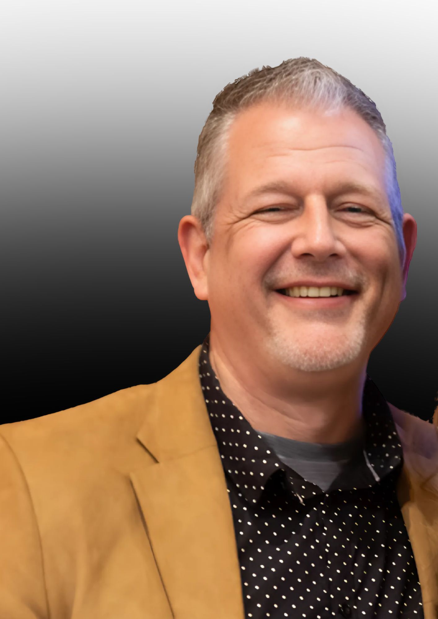 A man in a suit and polka dot shirt is smiling