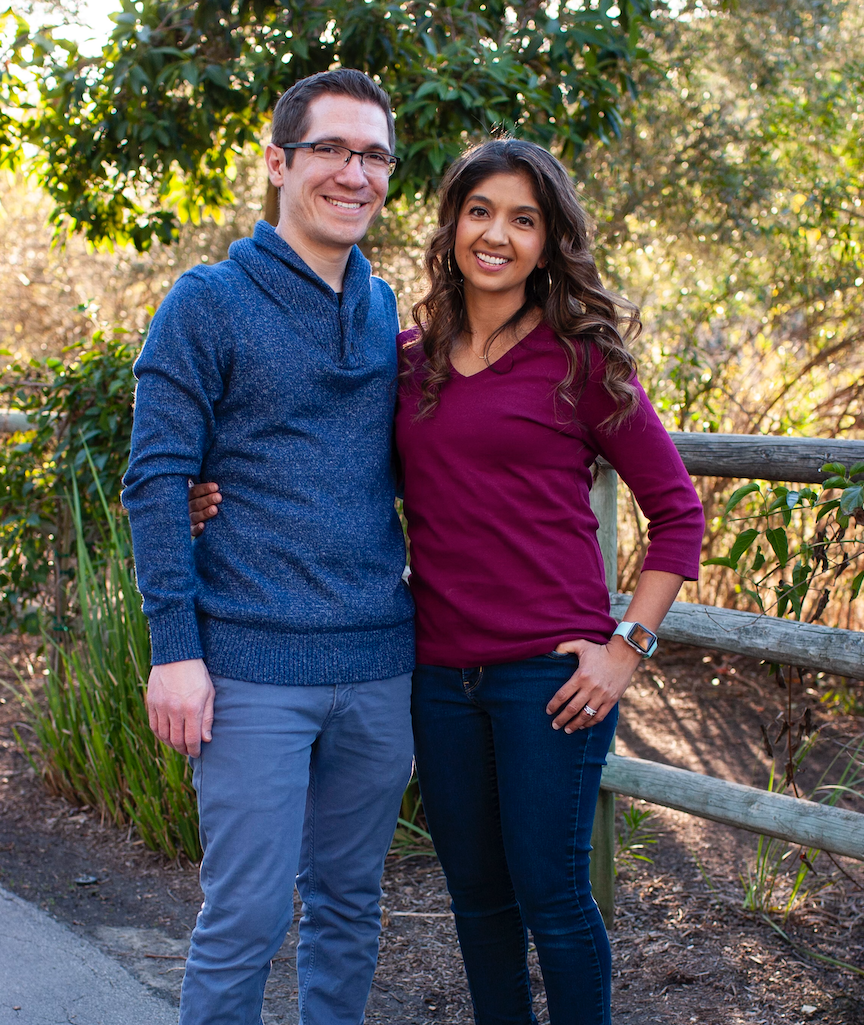 A man and a woman are posing for a picture in front of a wooden fence.