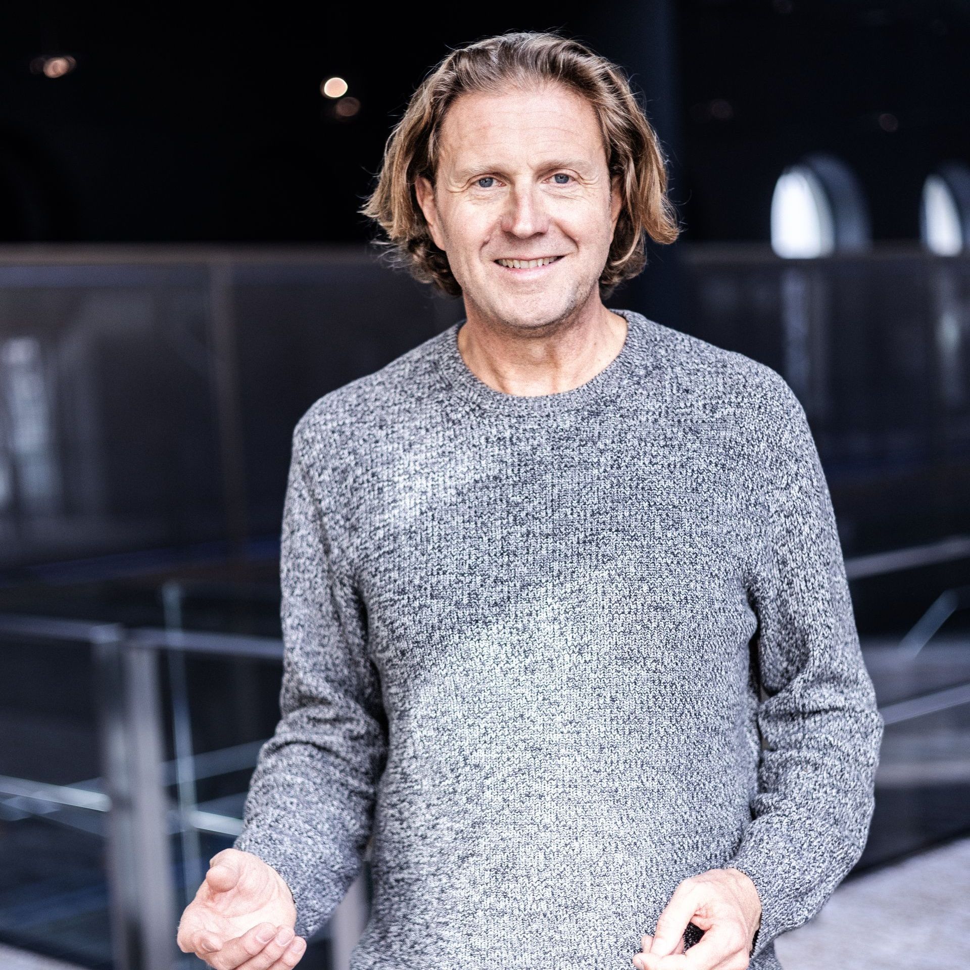 Ein Mann in einem grauen Pullover hebt seine Hand in die Luft