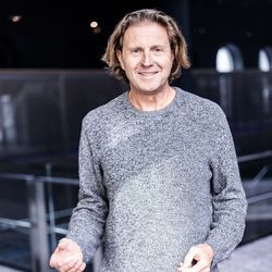 Ein Mann in einem grauen Pullover hebt seine Hand in die Luft