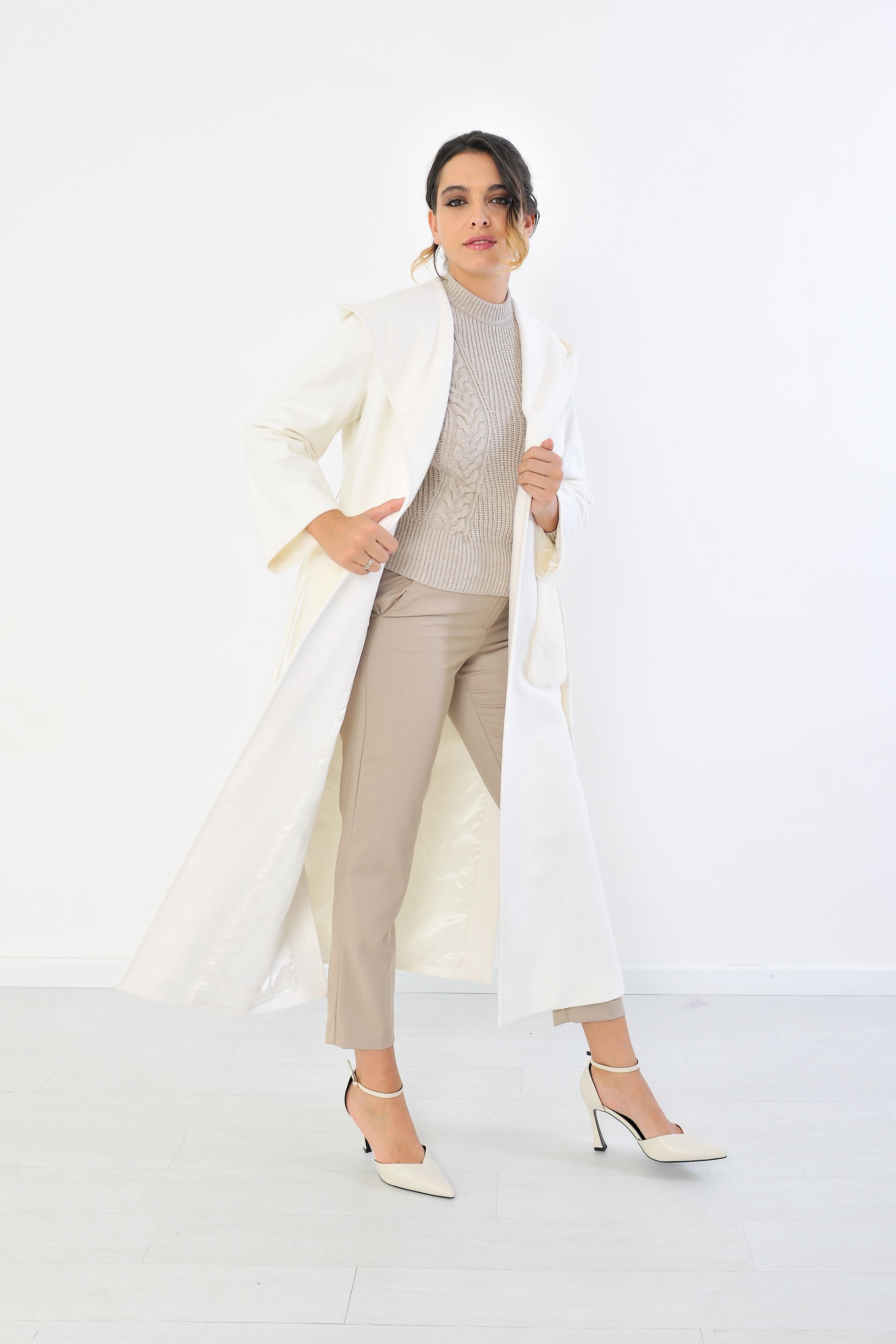 Donna in camice bianco, top beige fantasia, orecchini d'oro. Su sfondo bianco.