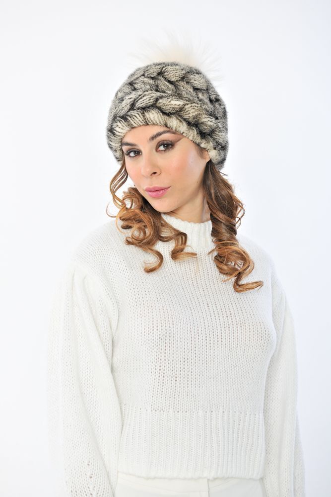 Donna che indossa un cappello fantasia e un maglione bianco, guarda in basso con un'espressione contemplativa.