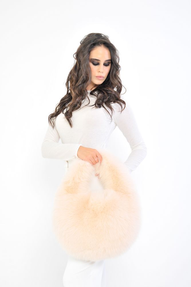 Una donna tiene davanti al viso un soffice accessorio di pelliccia color pesca, su uno sfondo bianco.