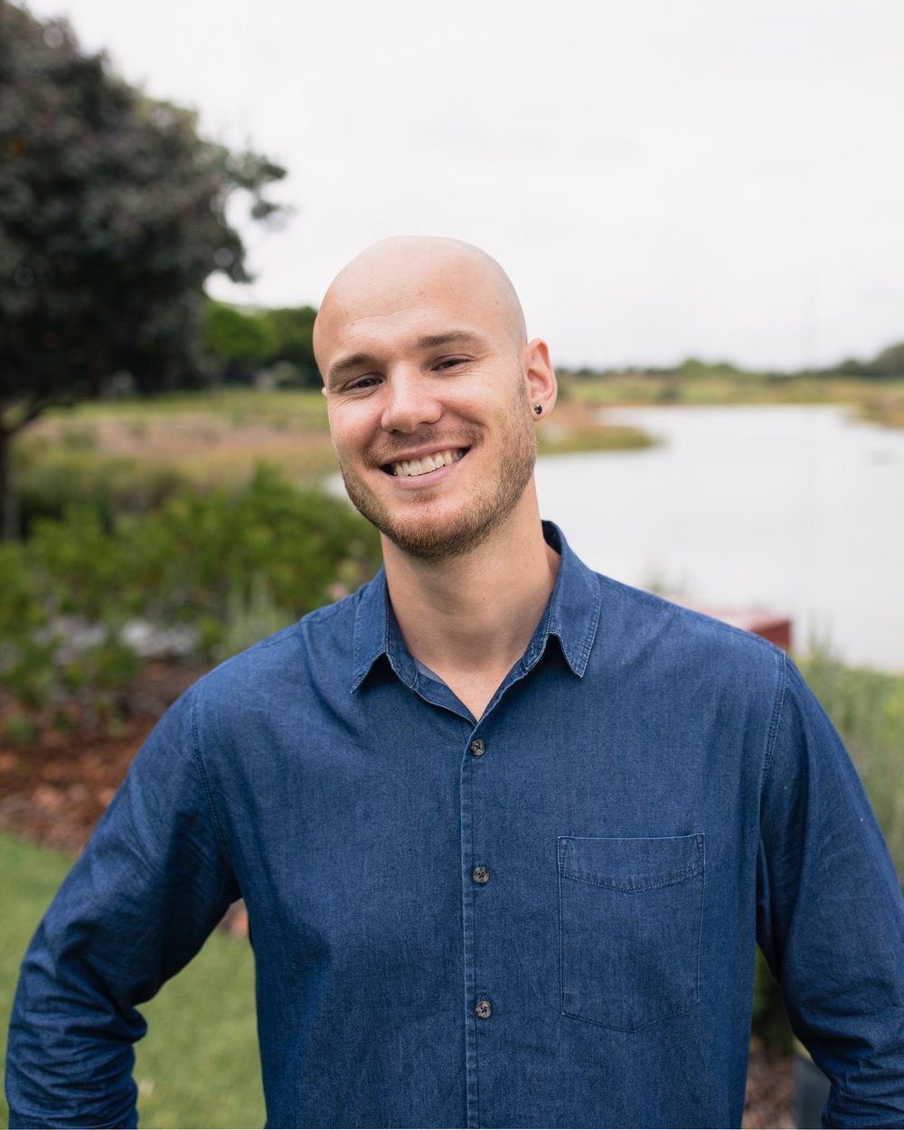 A Bald Man In A Blue Shirt Is Standing In Front Of A Body Of Water — St. John Imagery In Sydney, NSW