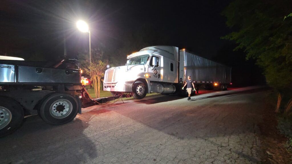 A semi truck is being towed down a road at night.