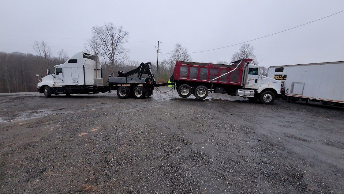 A dump truck is being towed by a semi truck in a parking lot.
