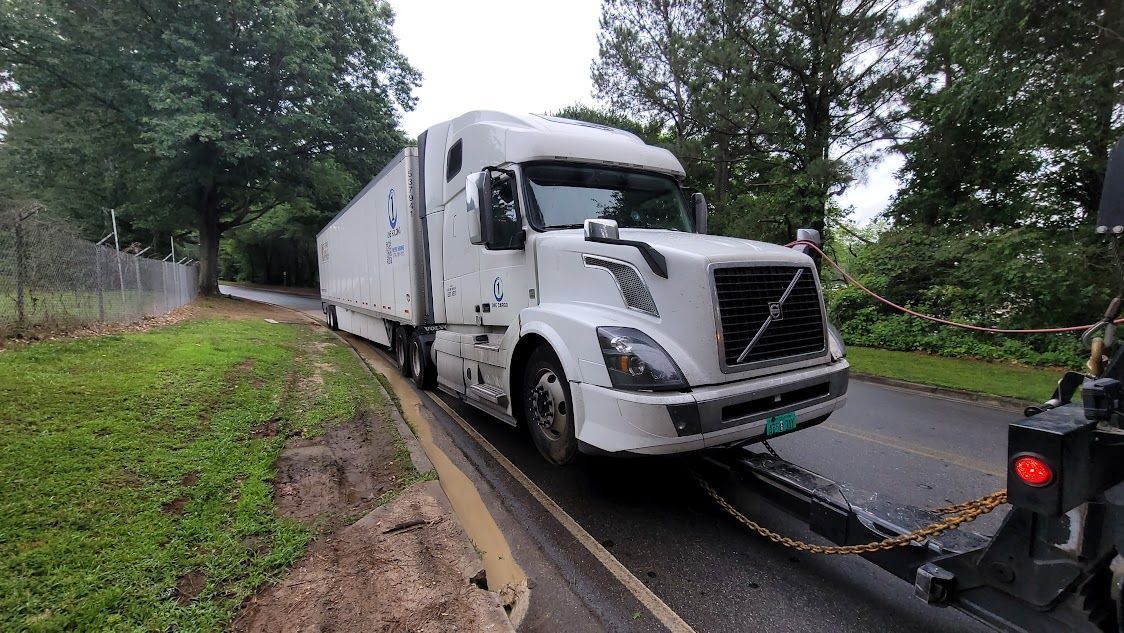 A white semi truck is being towed down a road by a tow truck.