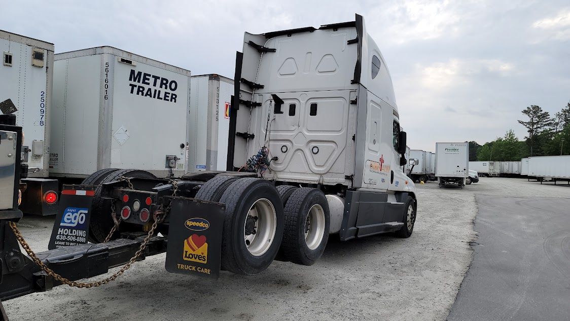 A semi truck with a trailer attached to it is parked in a lot.