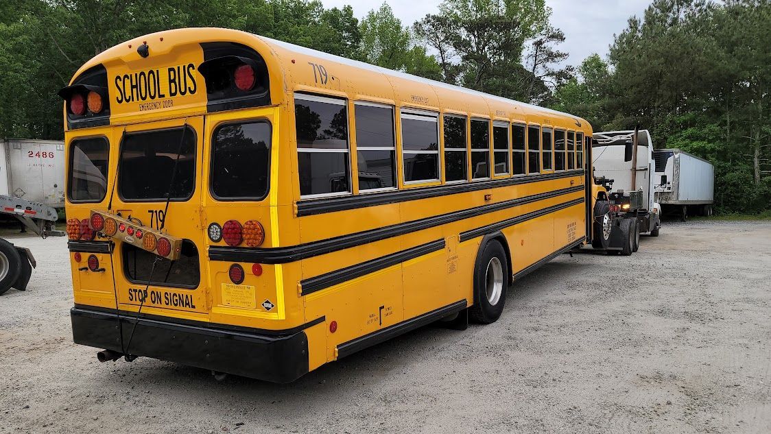 A yellow school bus is parked in a gravel lot.