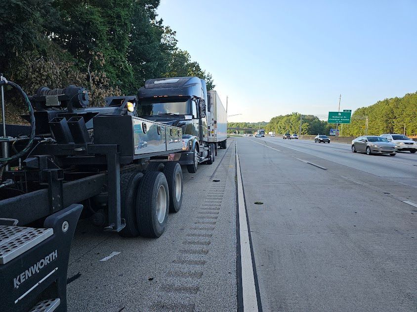 Two semi trucks are parked on the side of a highway.