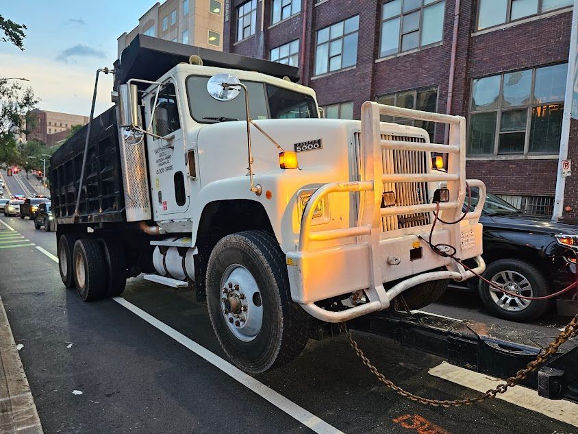 A white and black dump truck is parked on the side of the road.
