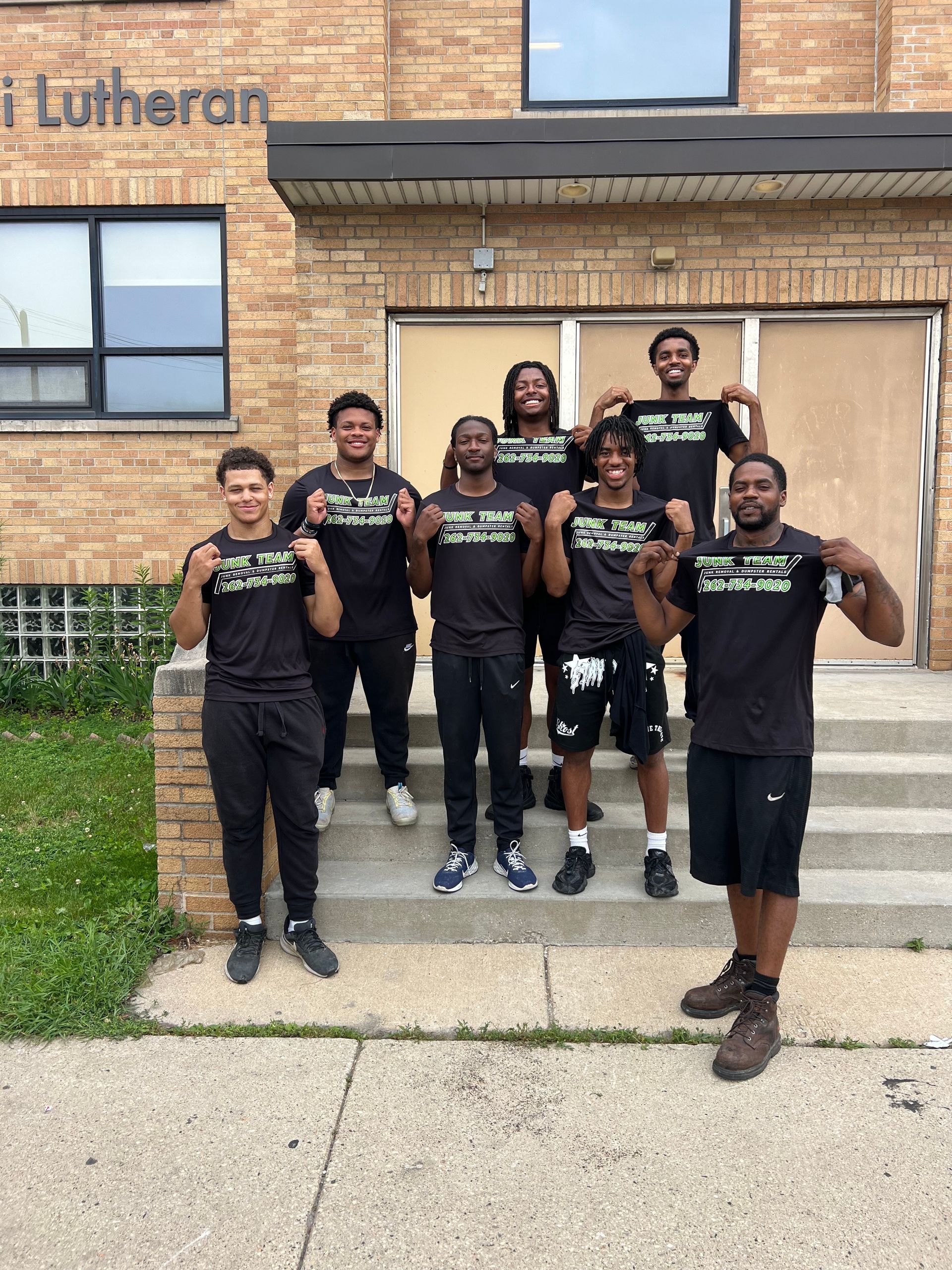 A group of young men are posing for a picture in front of a brick building.