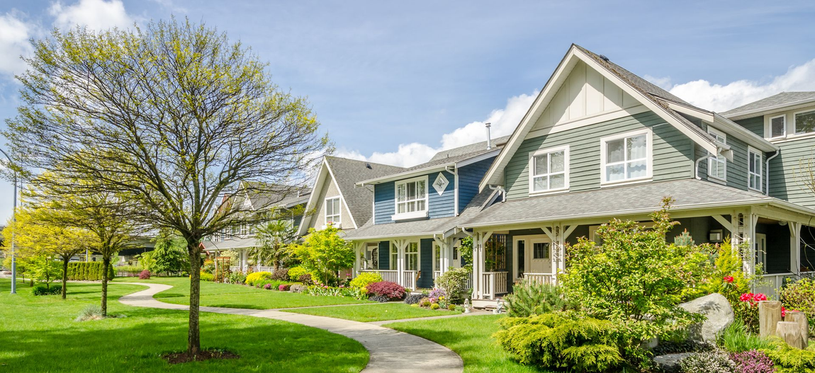 Row of houses with green lawns and a winding pathway under a blue sky.