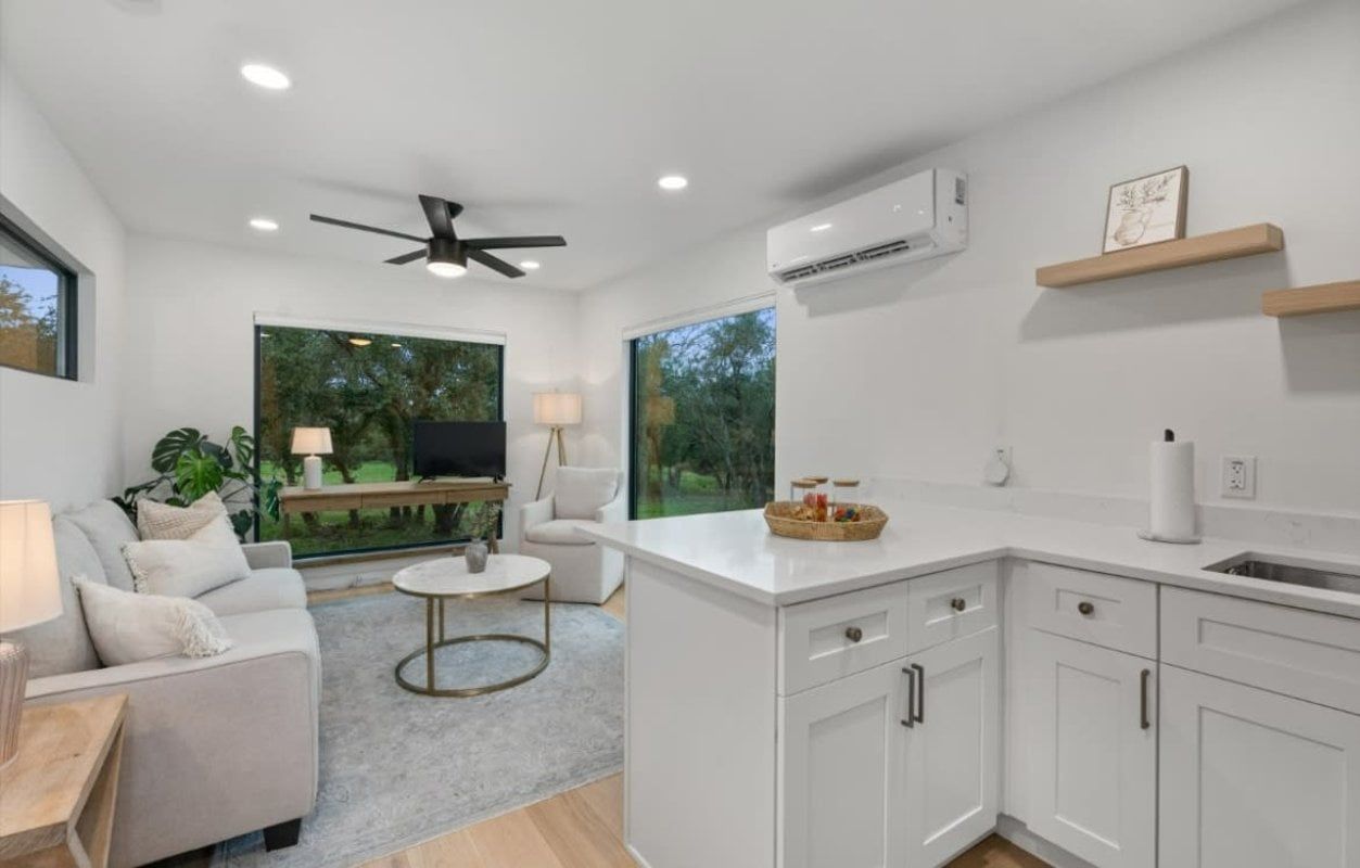 White-walled living space with kitchen and a view of greenery through large windows.