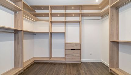 Empty walk-in closet with built-in wooden shelves, drawers, and hanging rods; dark wood floor.